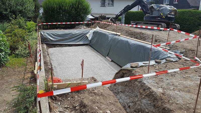 Ausgehobene Grube mit Vlies, Absperrband und Bagger