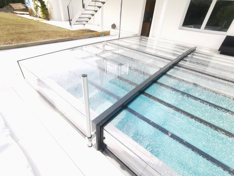 Pool unter einer flachen Glas-Überdachung neben einer Terrasse – ein Badipool-Projekt